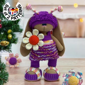 Könnte beinhalten: Ein gehäkeltes lila Kaninchen, das ein lila-weiß gestreiftes Kleid trägt und eine weiße Blume mit orangefarbener Mitte hält. Das Kaninchen trägt lila-weiß gestreifte Schuhe. Das Kaninchen steht auf einer Holzoberfläche. Das Bild enthält den Text "Set of 2 Patterns".