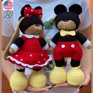 Pode incluir: Dois brinquedos de pelúcia de crochê, um vestido como Mickey Mouse e o outro como Minnie Mouse. O brinquedo Mickey Mouse está vestindo calças pretas com detalhes vermelhos, uma gravata borboleta amarela e sapatos pretos. O brinquedo Minnie Mouse está vestindo um vestido vermelho com bolinhas brancas e um laço branco com bolinhas vermelhas. Ambos os brinquedos têm orelhas pretas e rostos marrons.