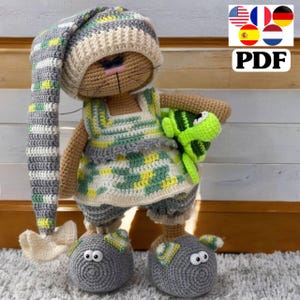 May include: A crocheted cat doll wearing a striped hat, a green and yellow dress, and gray slippers. The doll is holding a green crocheted turtle.