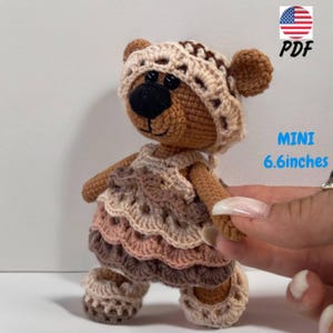 May include: A crocheted teddy bear wearing a crocheted hat and dress. The bear is brown with black eyes and a black nose. The dress is a multi-colored crocheted dress with a ruffled skirt. The bear is 6.6 inches tall.  PDF.