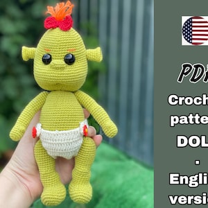 May include: A crochet pattern for a green troll doll wearing a white diaper with red flowers. The pattern is in PDF format and is in English. The image also includes a small American flag.
