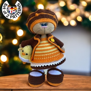 Może przedstawiać: Pluszowa lalka kota w brązowej i pomarańczowej czapce, brązowej kurtce i żółto-pomarańczowej sukience. Lalka trzyma małego, pluszowego, żółtego kurczaka. Lalka stoi na drewnianej powierzchni.