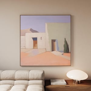 May include: A framed abstract painting depicts a minimalist architectural scene. The artwork features white and pale green buildings with brown doorways, set against a peach-colored ground and a pale blue sky. A small green tree is visible.