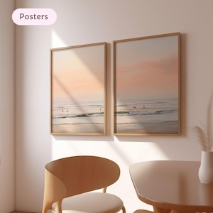 May include: Two framed beach scene posters. The artwork depicts a serene ocean view with surfers and a pastel sunset. The frames are a light wood color, and the posters are displayed on a neutral-colored wall. The word "Posters" is in a pink oval in the upper left corner.