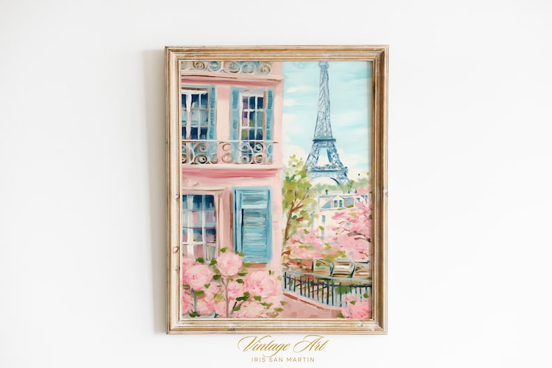 Pu&ograve; includere: Un dipinto che raffigura un edificio rosa con persiane blu e un balcone, con la Torre Eiffel sullo sfondo. L'edificio &egrave; circondato da fiori rosa e alberi. Il dipinto &egrave; incorniciato in una cornice di legno chiaro. Vintage Art di Iris San Martin.