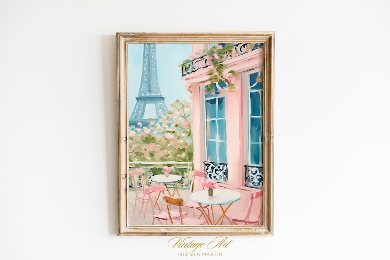 May include: A painting of a Parisian cafe with pink walls and a view of the Eiffel Tower. The cafe has tables and chairs on the patio, with pink flowers and greenery. The painting is framed in a light wood frame.