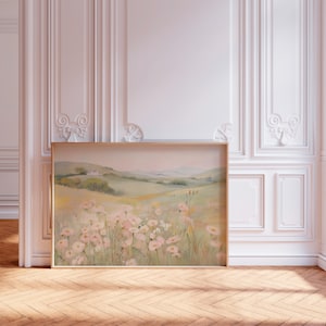 May include: A framed landscape painting depicting a field of pink flowers, green hills, and a distant house. The artwork is displayed in a room with white panelling and a wooden floor. The painting's frame is made of wood.