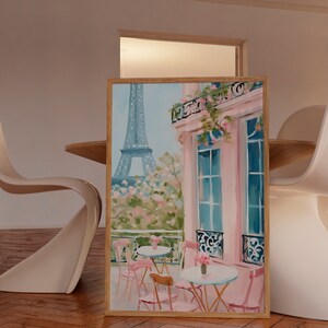 May include: A painting of a Parisian cafe with pink walls and a view of the Eiffel Tower. The cafe has tables and chairs with pink cushions. There are flowers on the tables and in the window boxes.