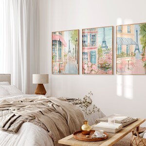 May include: Three framed watercolor paintings depicting a Parisian street scene with the Eiffel Tower in the background. The paintings feature a cafe with pink tables and chairs, a building with a pink awning, and blooming pink flowers.