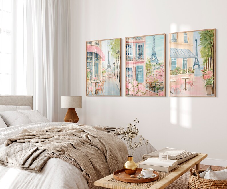 May include: Three framed watercolor paintings depicting a Parisian street scene with the Eiffel Tower in the background. The paintings feature a cafe with pink tables and chairs, a building with a pink awning, and blooming pink flowers.