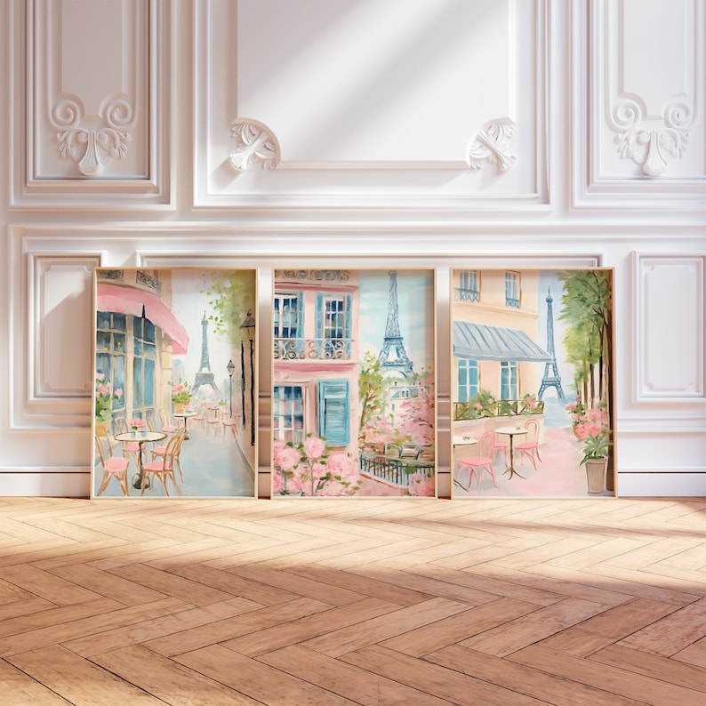 May include: Three framed watercolor paintings depicting Parisian street scenes. Each painting features a pink building with a blue awning, a cafe with tables and chairs, and the Eiffel Tower in the background. The paintings are set against a white wall with ornate moldings.