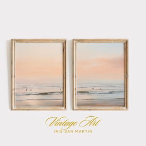 May include: Two framed beach art prints. Each print depicts a serene ocean scene with surfers, under a pastel sunset sky. The frames are a light wood color, adding a vintage aesthetic to the artwork.