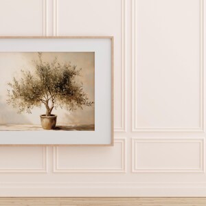 May include: A framed print of an olive tree in a terracotta pot. The artwork is set against a neutral background, with a light wood frame. The wall is painted a soft pink with decorative molding.