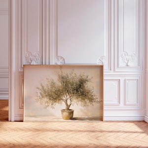 May include: A framed artwork featuring an olive tree in a terracotta pot. The painting has a soft, muted color palette with shades of green and brown. The artwork is displayed against a white wall with decorative molding, and a wooden floor.