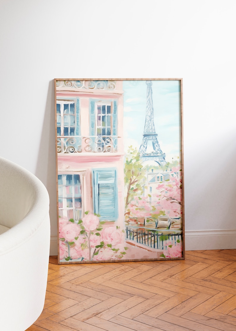 Pu&ograve; includere: Un dipinto incorniciato di un edificio rosa con persiane blu e un balcone che si affaccia su una scena di strada a Parigi, Francia. La Torre Eiffel &egrave; visibile sullo sfondo, e ci sono fiori rosa in primo piano.