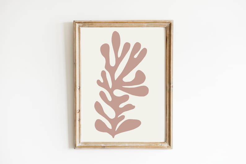 May include: Framed abstract art print featuring a coral-colored botanical design on an off-white background. The artwork is enclosed in a rustic, light brown wooden frame, creating a minimalist aesthetic. Ideal for home decor.