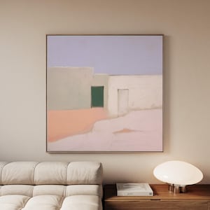 May include: Abstract painting featuring a minimalist architectural scene. The artwork depicts white buildings with a green door and a light blue sky. The color palette includes soft pink and beige tones, framed in a simple wooden frame.