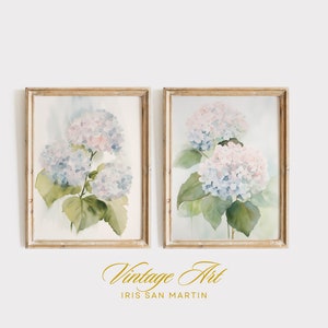 May include: Two framed watercolor prints featuring hydrangea blooms in soft blue and pink hues, with green leaves. The prints are in gold-toned frames. The text "Vintage Art" and the artist's name are at the bottom.
