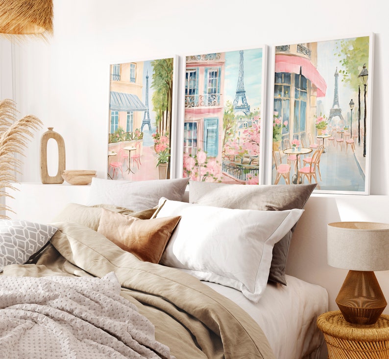 May include: Three framed watercolor paintings depicting Parisian street scenes with pink and blue hues. The paintings feature cafes, flowers, and the Eiffel Tower.