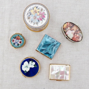 Może przedstawiać: Kolekcja ozdobnych pudełek w stylu vintage. Pudełka obejmują okrągły kwiatowy wzór, mozaikowy kwiatowy wzór, niebieskie marmurowe kwadratowe pudełko, owalne pudełko z obrazem, niebieski kwiatowy wzór i kwadratowe pudełko z masy perłowej.