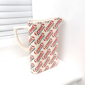Peut inclure: Pichet crème avec une anse et un bec verseur incurvés. Le pichet est recouvert d'un motif répété avec les mots "Grant's Scotch Whisky" en rouge. Fabriqué en céramique ou porcelaine.
