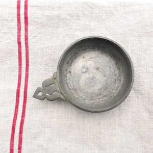 May include: A silver-coloured metal bowl with a decorative handle. The bowl is round and has a smooth, slightly worn surface.