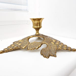 May include: A vintage brass candle holder with a leaf-shaped base. The candle holder has a detailed design with a central cup for the candle and a decorative leaf pattern. The brass has a warm, aged patina.