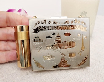 May include: A square silver-toned metal compact case featuring gold-toned engravings of Washington D.C. landmarks including the Capitol, Washington Monument, and Jefferson Memorial, with an attached cylindrical gold-toned lipstick holder case.