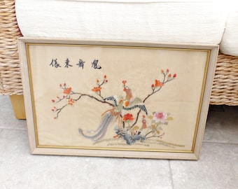 May include: A framed embroidery depicting two colorful birds perched on a flowering branch. The embroidery is on a cream-colored fabric and includes the Chinese characters "松鶴長春".