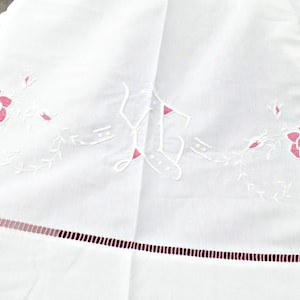 Pode incluir: Toalha de mesa de linho branco bordada com uma inicial "L" bordada em rosa e desenhos florais.