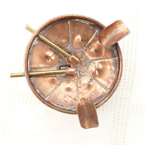 May include: A copper ashtray with three brass cigarette holders. The ashtray has a decorative design and is in good condition.
