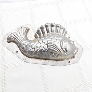 May include: A vintage metal mould shaped like a fish. The mould is silver in colour and has a detailed design of scales and fins.