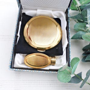 May include: A gold compact mirror and a gold compact case in a blue and white patterned box. The mirror and case have a textured, diamond-shaped pattern.