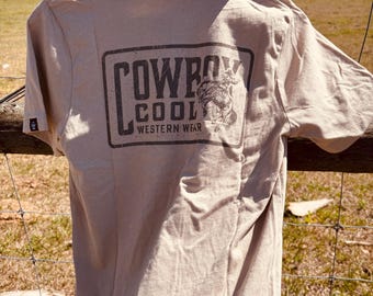 May include: A tan t-shirt with a black and white graphic of a cowboy with the text "COWBOY COOL WESTERN WEAR" on the back.