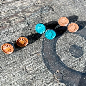 May include: Six small, round earrings with a starburst design. Three earrings are turquoise blue and three are brown.