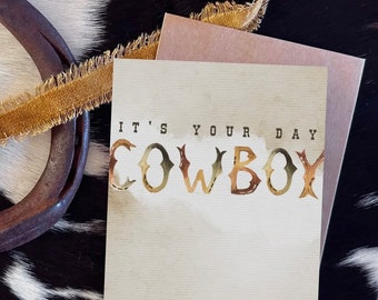 May include: A card with a rustic background and the text "It's your day Cowboy" in gold letters. The letters are made of horseshoes.