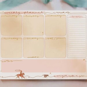 May include: Weekly planner notepad with a light pink and beige color scheme. The notepad features sections for each day of the week, a to-do list, and a notes section. A cowgirl illustration and the text "a cowgirl with a plan" are at the bottom.