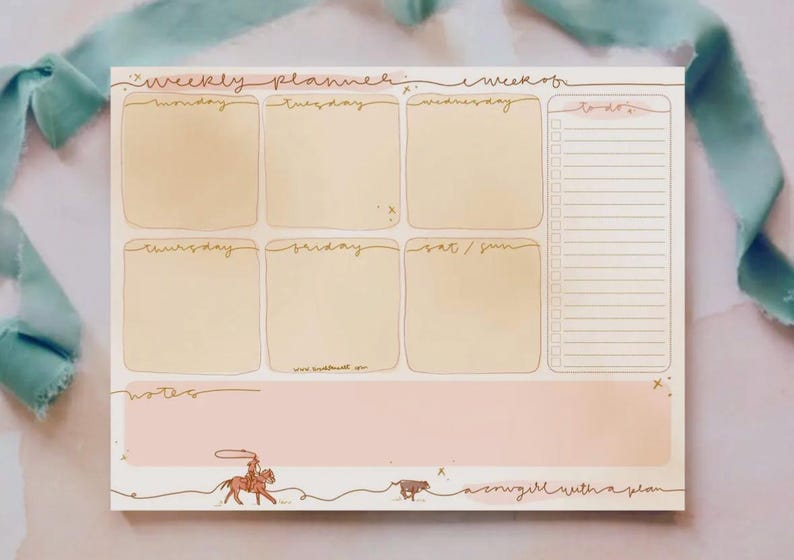 May include: Weekly planner notepad with a light pink and beige color scheme. The notepad features sections for each day of the week, a to-do list, and a notes section. A cowgirl illustration and the text "a cowgirl with a plan" are at the bottom.