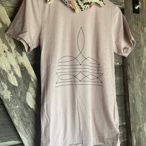May include: A light pink t-shirt with a black geometric design on the front. The design is a stylized image of a flower or a star.