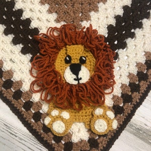 Op de afbeelding: Een gehaakte leeuwenapplicatie in bruin, wit en beige. De leeuw heeft een pluche manen en een vriendelijke uitdrukking.