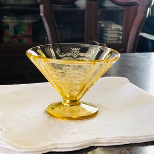 May include: A yellow glass dessert dish with a decorative pattern. The dish is on a white napkin.