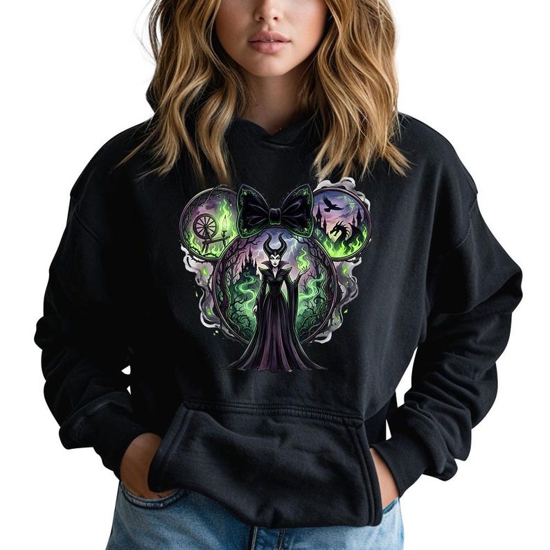 May include: Black hooded sweatshirt with a Disney villain graphic. The design incorporates a castle silhouette, a spinning wheel, and a dragon, arranged in a Mickey Mouse ear shape. The villain is shown in a long black dress.