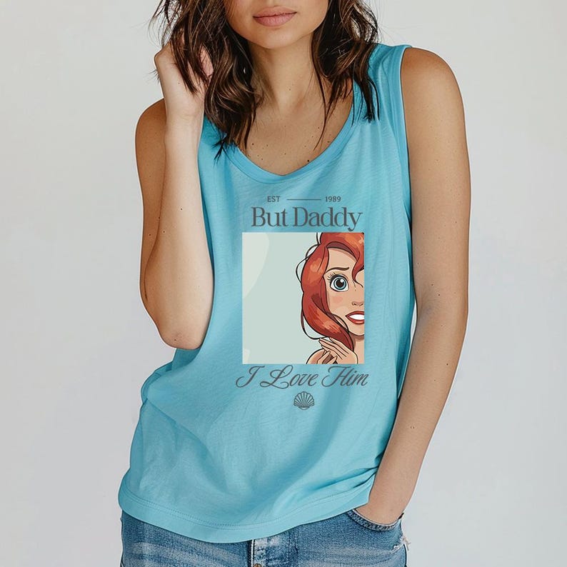 May include: A light blue tank top with a scoop neck. The shirt features a graphic of a cartoon character with red hair and the text "But Daddy" above the image and "I Love Him" below it.