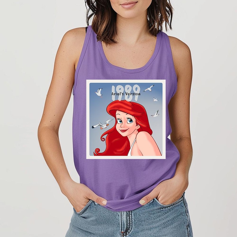 May include: A purple tank top featuring a graphic of Ariel from The Little Mermaid. The graphic includes the text "1989 Ariel's Version" with Ariel's image and seagulls against a blue sky background.