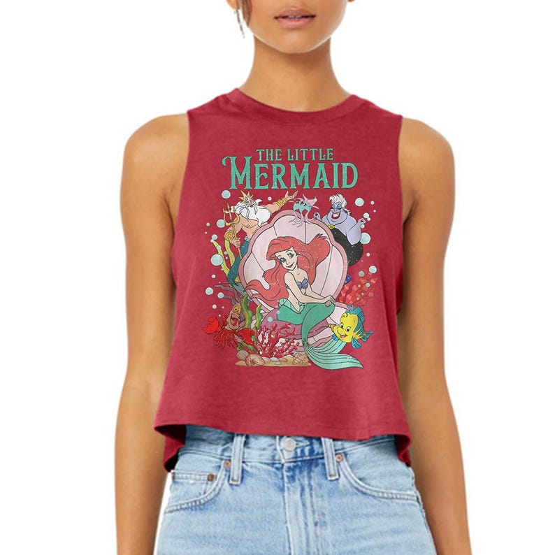 Puede incluir: Un top corto sin mangas de color granate con un estampado gr&aacute;fico de los personajes de La Sirenita, incluyendo a Ariel, el Rey Trit&oacute;n, &Uacute;rsula, Sebasti&aacute;n y Flounder. El texto THE LITTLE MERMAID est&aacute; impreso en color cerceta sobre los personajes.