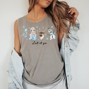 May include: A gray tank top featuring a graphic of Elsa, Sven, and Olaf from the movie Frozen, with snowflakes and the text "Let it go". The sleeveless shirt is made of a soft material.