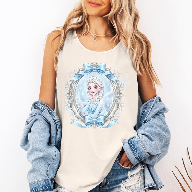 May include: Cream-colored tank top featuring a cartoon illustration of a woman with blonde hair and a blue dress, framed by a light blue oval with bows and snowflakes. The tank top is sleeveless.