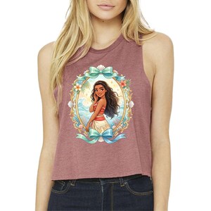 Puede incluir: Un top corto granate con una colorida ilustraci&oacute;n de una mujer en un entorno tropical. La ilustraci&oacute;n est&aacute; enmarcada por un &oacute;valo decorativo con detalles florales y lazos. La mujer tiene el pelo largo y oscuro y lleva un atuendo rojo y blanco.