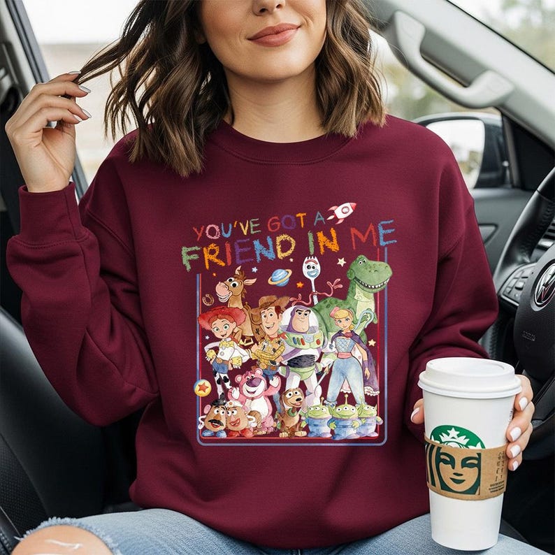 May include: Burgundy sweatshirt featuring a colorful graphic of characters from the Toy Story movie, including Woody, Buzz Lightyear, and Rex. The text "YOU'VE GOT A FRIEND IN ME" is above the graphic. The sweatshirt is a crew neck style.