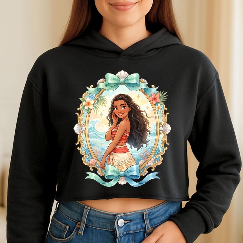 K&ouml;nnte beinhalten: Schwarzer Cropped-Hoodie mit einer farbenfrohen Illustration einer Frau in einem ovalen Rahmen. Der Rahmen ist mit Muscheln, Blumen und einem blauen Band verziert. Die Frau hat dunkles Haar und tr&auml;gt ein rot-wei&szlig;es Outfit.